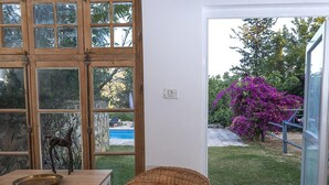 Une pièce avec une table en bois et une chaise en osier, une grande fenêtre donnant sur une piscine et un jardin.