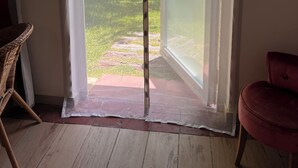 Une pièce dotée d’une porte-fenêtre coulissante donnant sur un jardin avec une piscine, une chaise en osier et une chaise rouge.