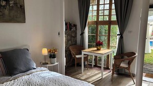 Une chambre à coucher avec un lit, une petite table avec une lampe, une chaise et une fenêtre avec des rideaux.