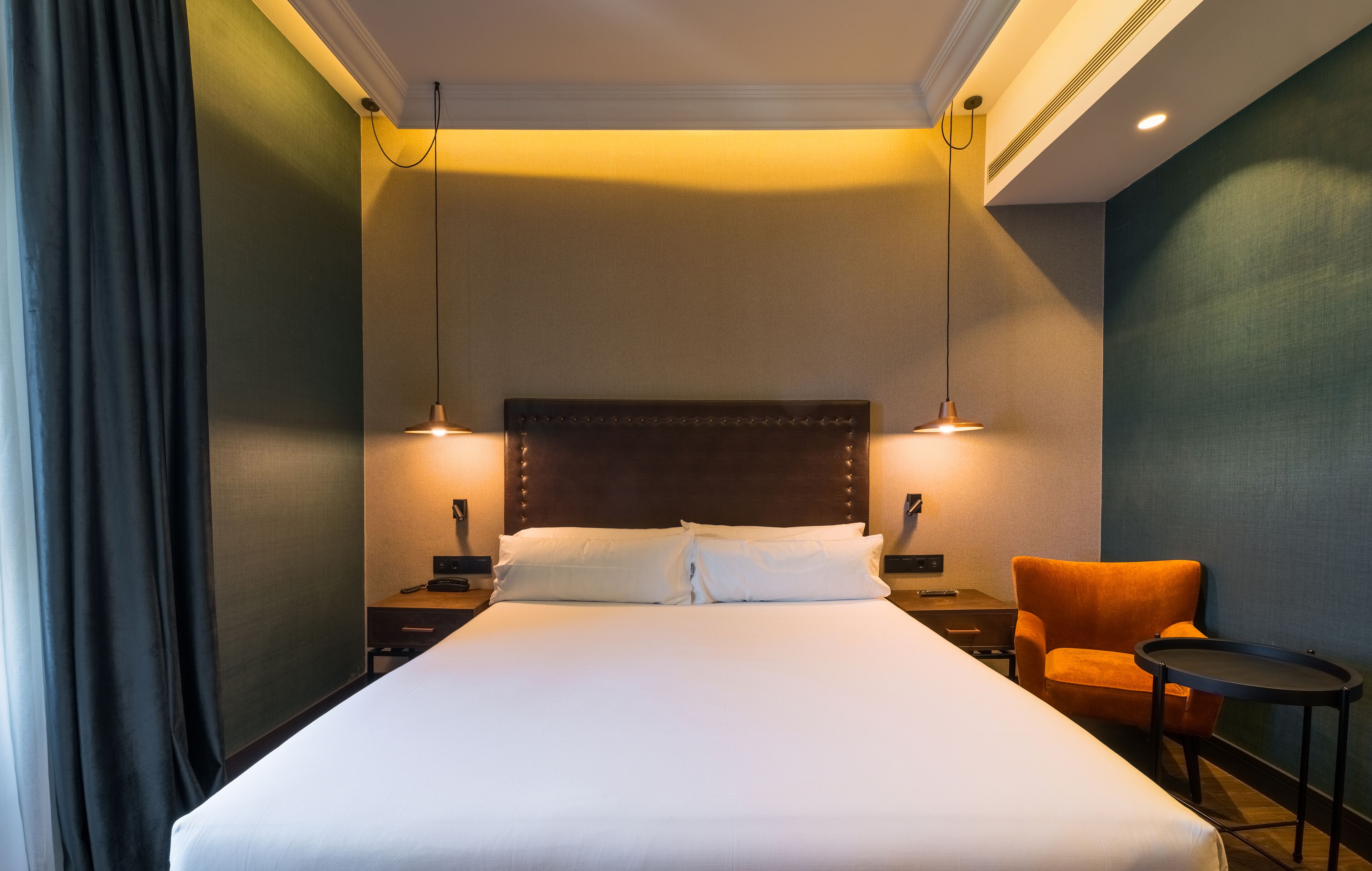 Habitación de hotel con una cama grande, dos mesitas de noche, una silla y una pequeña mesa.