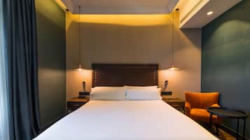 Habitación de hotel con una cama grande, dos mesitas de noche, una silla y una pequeña mesa.