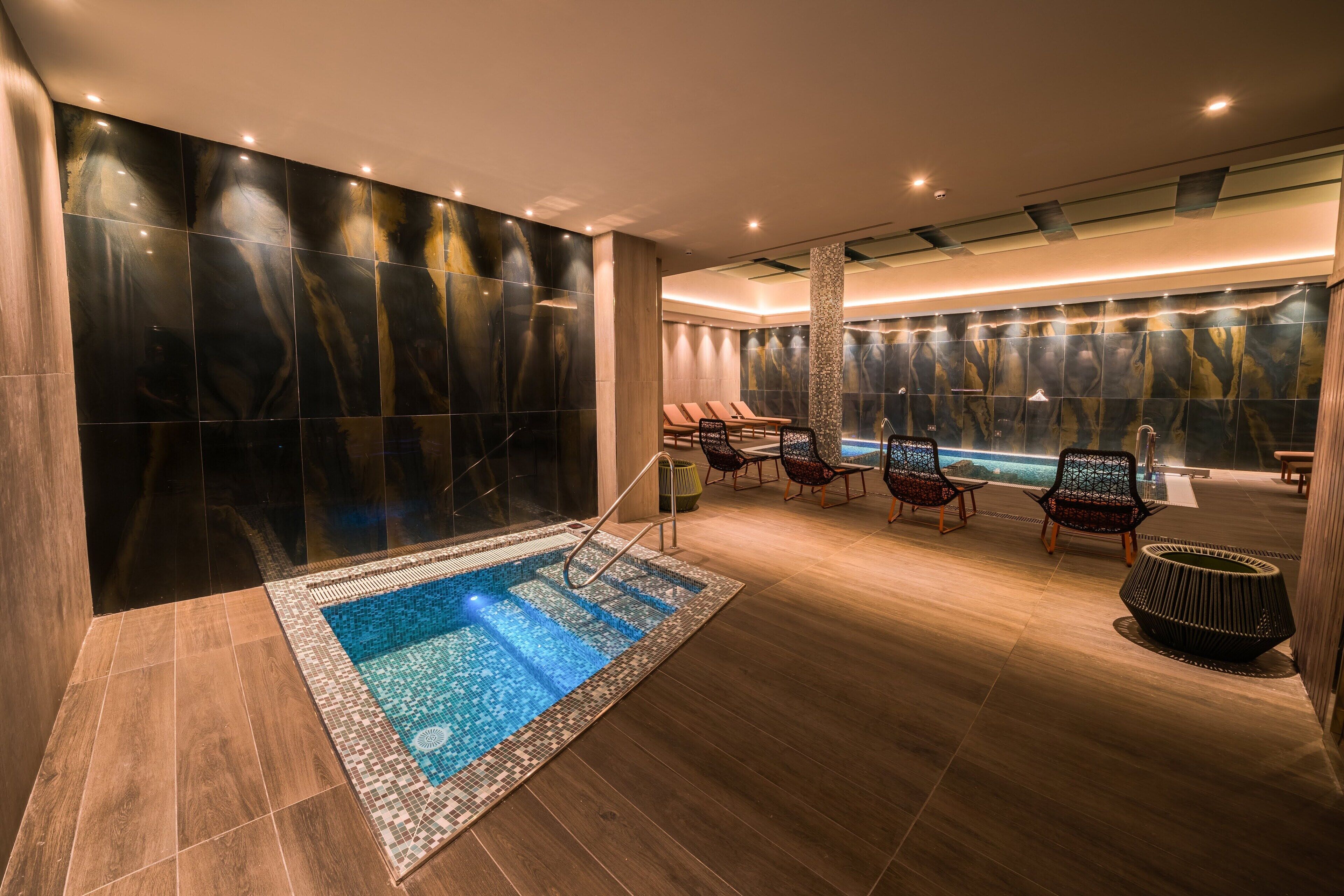 A modern spa area with a hot tub, lounge chairs, and a pool.