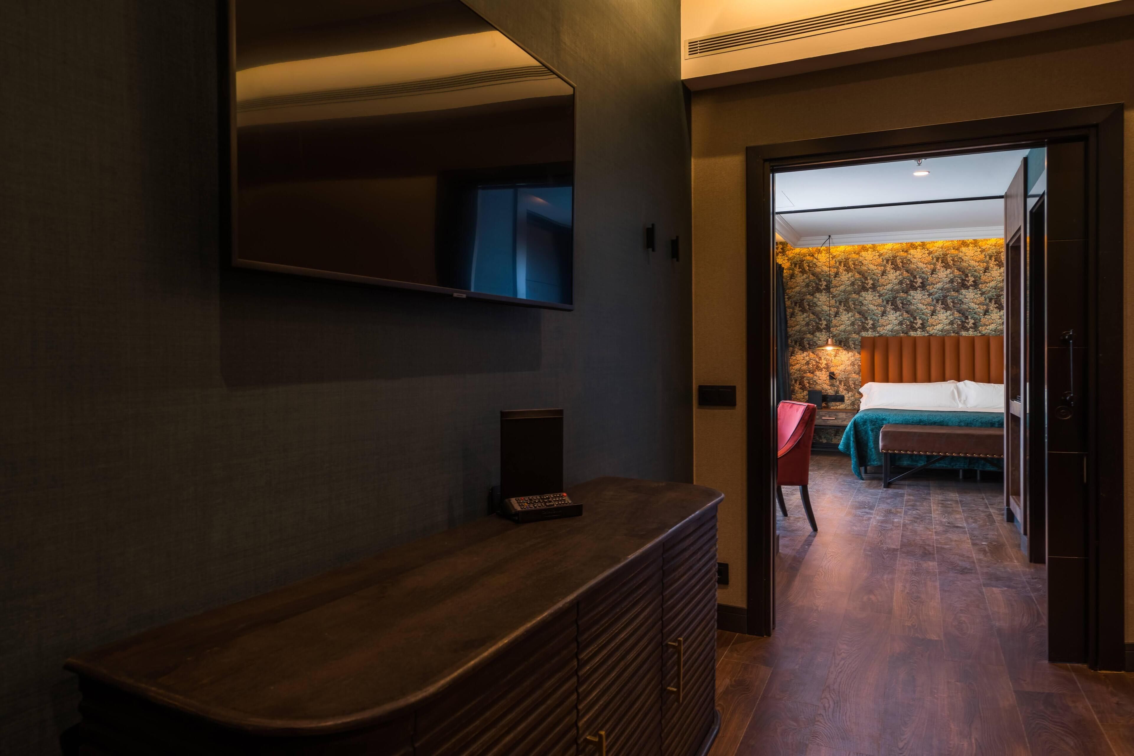 Habitació d'hotel amb una taula de consola de fusta, un televisor de pantalla plana fixat a la paret i un llit amb estriat verd i cortines taronges.