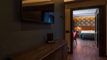 Habitació d'hotel amb una taula de consola de fusta, un televisor de pantalla plana fixat a la paret i un llit amb estriat verd i cortines taronges.