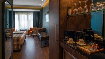 Una habitación de hotel con una cama, dos sillas, una mesita, un sofá, una zona de café y una vitrina con copas y botellas de vino.