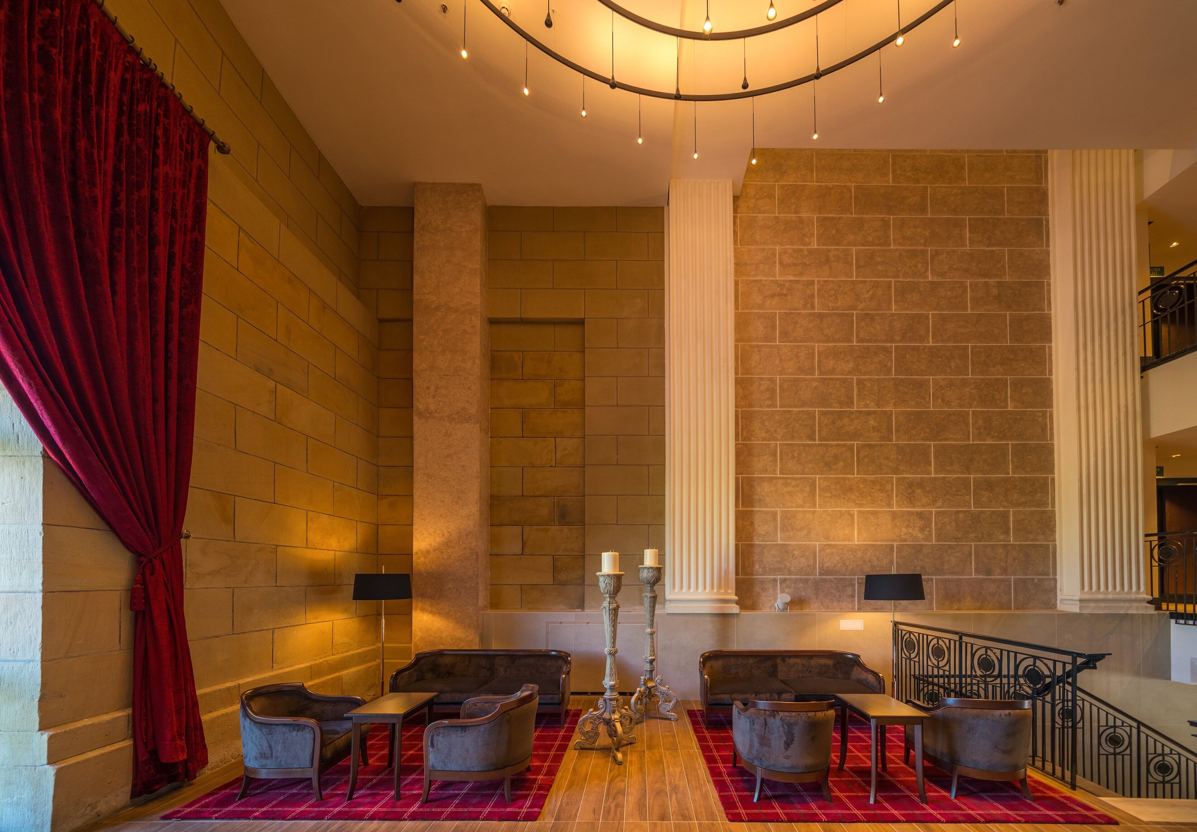 A lobby with a red carpet, two armchairs, a table, a candelabra, and a staircase.
