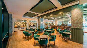 Un restaurante moderno con sillas y mesas verdes, una zona de bar y una cocina al fondo.
