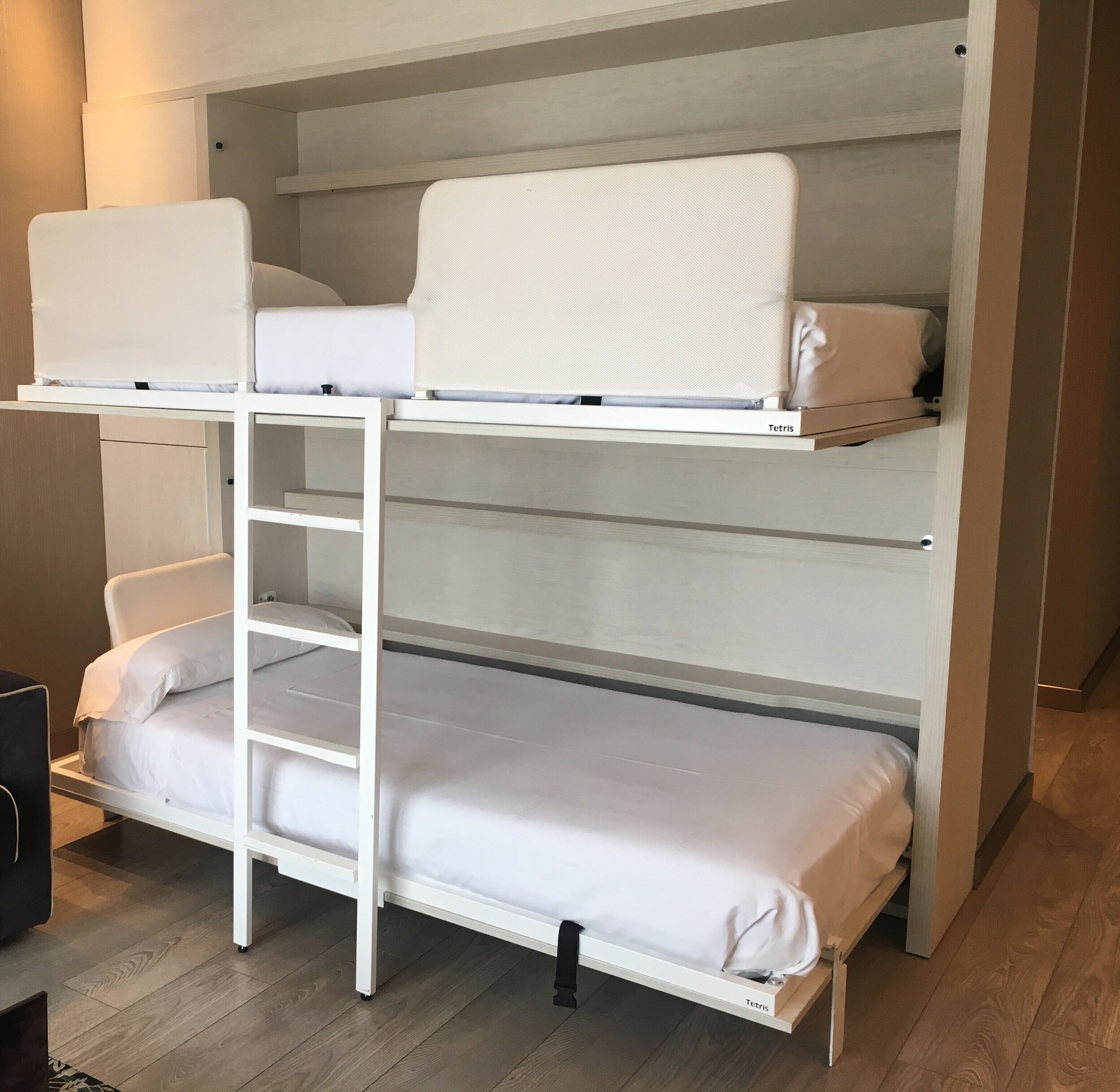 Una cama litera con escalera, ropa de cama blanca y un estante sobre la cama superior.
