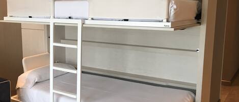 Una cama litera con escalera, ropa de cama blanca y un estante sobre la cama superior.