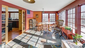 A sunlit dining area with a table and chairs, a large window with a view, and an American flag. - Charming Lovell Farmhouse - 17 Acres w/ Mtn Views! (Lovell)