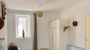 A bedroom with a bed, a chair, a wardrobe, a radiator, and a window with curtains. - 5/8 person gîte close to the landing beaches (Moulins en Bessin)