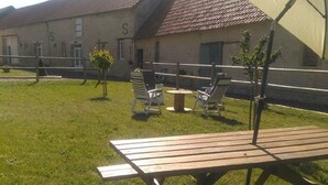 A picnic table with chairs in a grassy outdoor area, a building with a tiled roof, and a large umbrella. - 5/8 person gîte close to the landing beaches (Moulins en Bessin)
