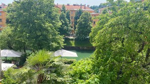A lush garden with trees and a body of water, surrounded by buildings. - Ljubljana centre, river view, balcony & bikes (Ljubljana)