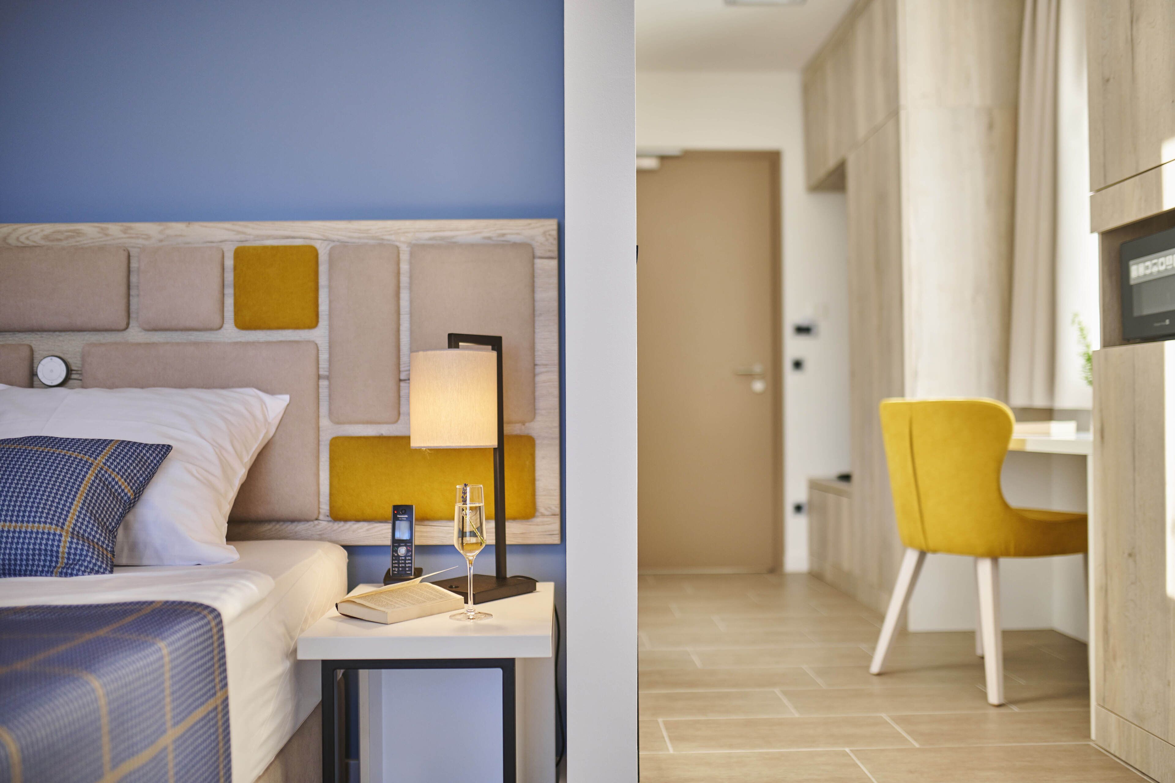 A modern hotel room with a bed, bedside table, lamp, and a small bedside clock.