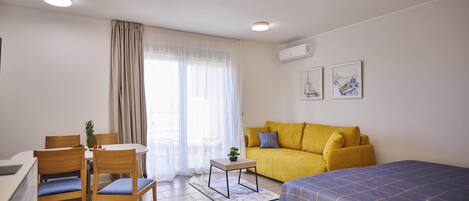 A modern room with a bed, a sofa, a dining table with chairs, and a small table with a plant.