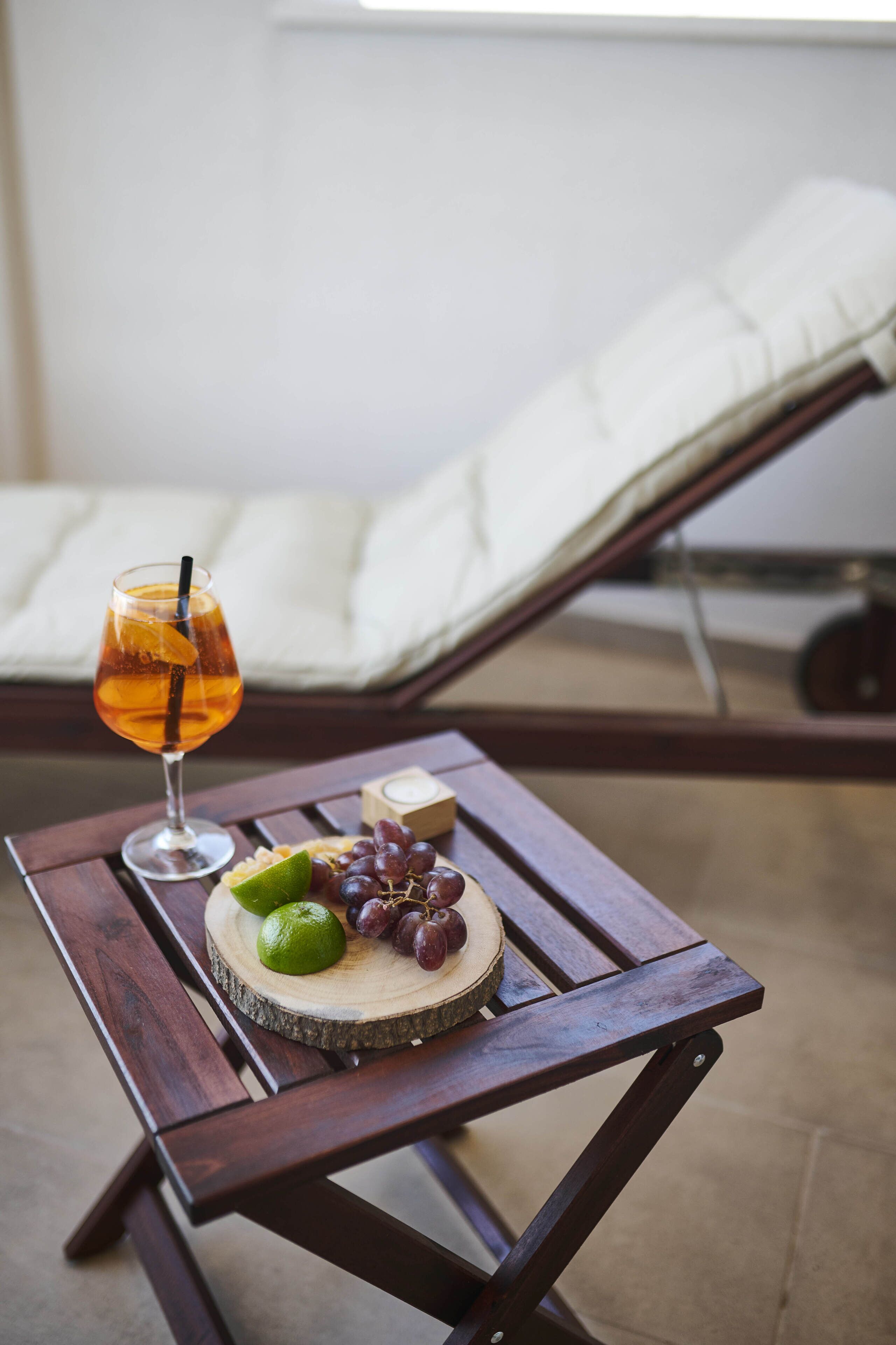 Una mesa de madera con un vaso de bebida color ámbar, lima, uvas y una pequeña vela.