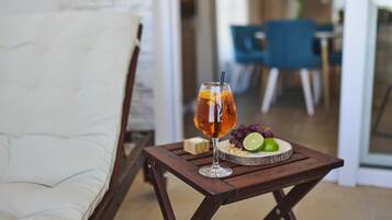 A glass of amber-colored beverage on a wooden tray with a lime and grapes, placed on a small table in a room with a white couch and blue chairs.