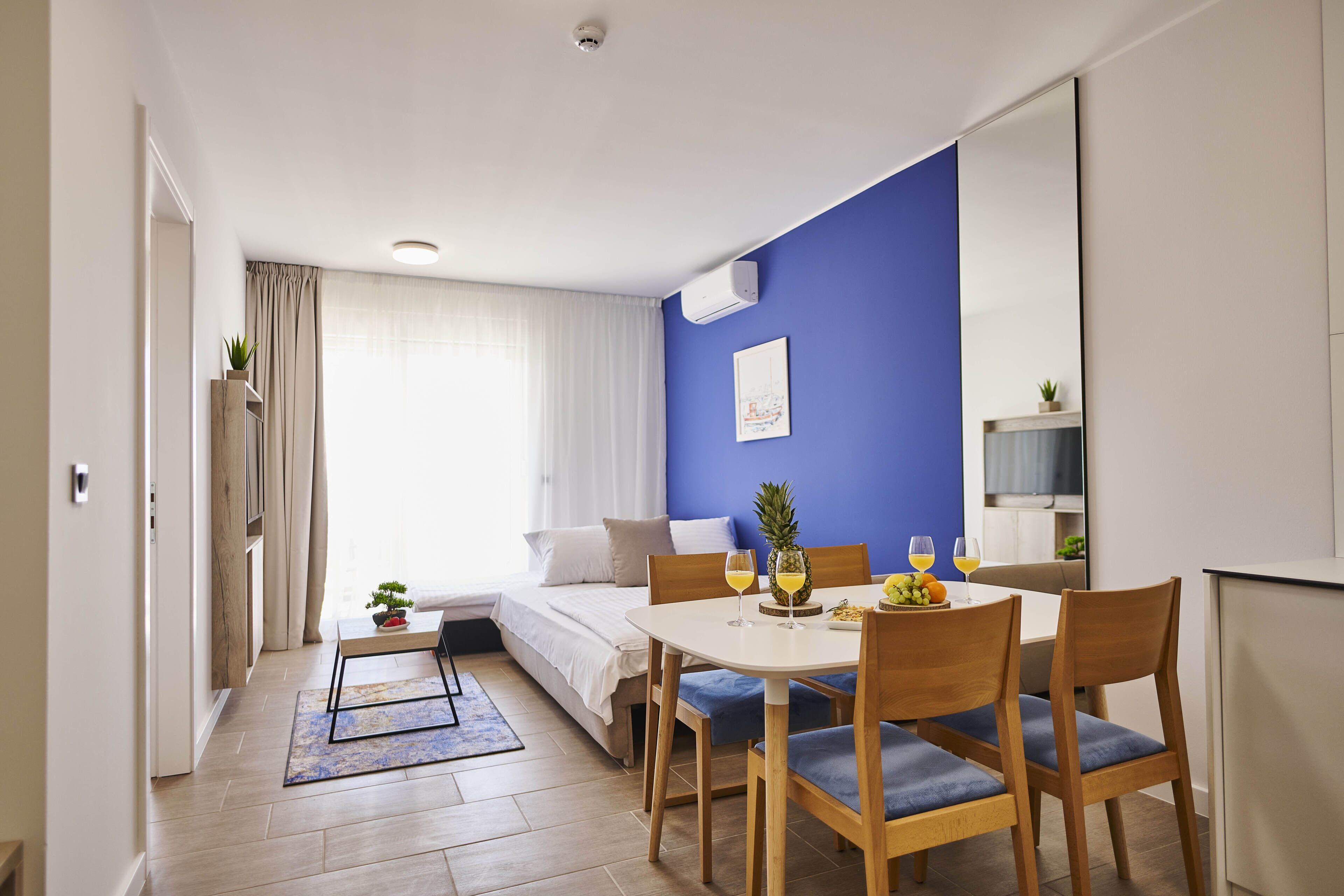 Una habitación de hotel moderna con una cama, una mesa de comedor con sillas, una planta pequeña y un frutero.