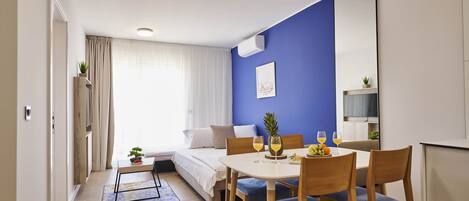 Una habitación de hotel moderna con una cama, una mesa de comedor con sillas, una planta pequeña y un frutero.