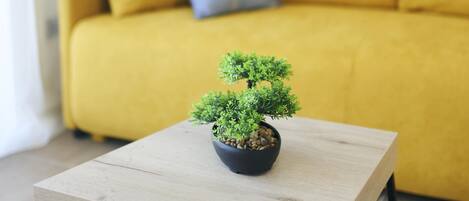 A small potted plant on a wooden table in a room with a yellow sofa and a framed picture on the wall.