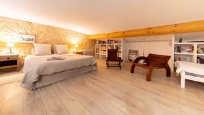 Une chambre à coucher comprenant un lit, des tables de chevet, une chaise, une bibliothèque et une poutre en bois au plafond.