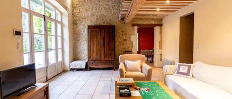 A spacious living room with a stone wall, wooden ceiling beams, a television, a sofa, and a coffee table with books.