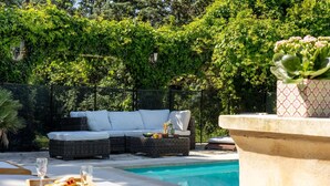 Un espace aménagé au bord de la piscine, avec un canapé en osier, une table à manger sur laquelle sont disposés un plateau de nourriture et de boissons, et une fontaine.