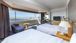 Habitación de hotel con dos camas, un escritorio, una silla, un televisor y vista a la ciudad.