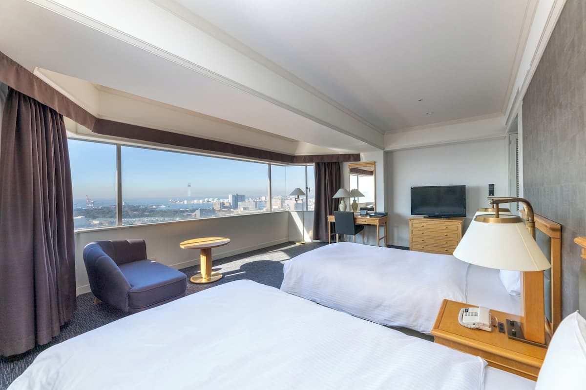 Une chambre d’hôtel avec deux lits, un bureau, une chaise, une télévision et une vue sur la ville.