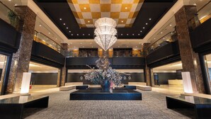 Un lobby amplio con una lámpara decorativa en el centro, columnas de mármol y un techo a cuadros.