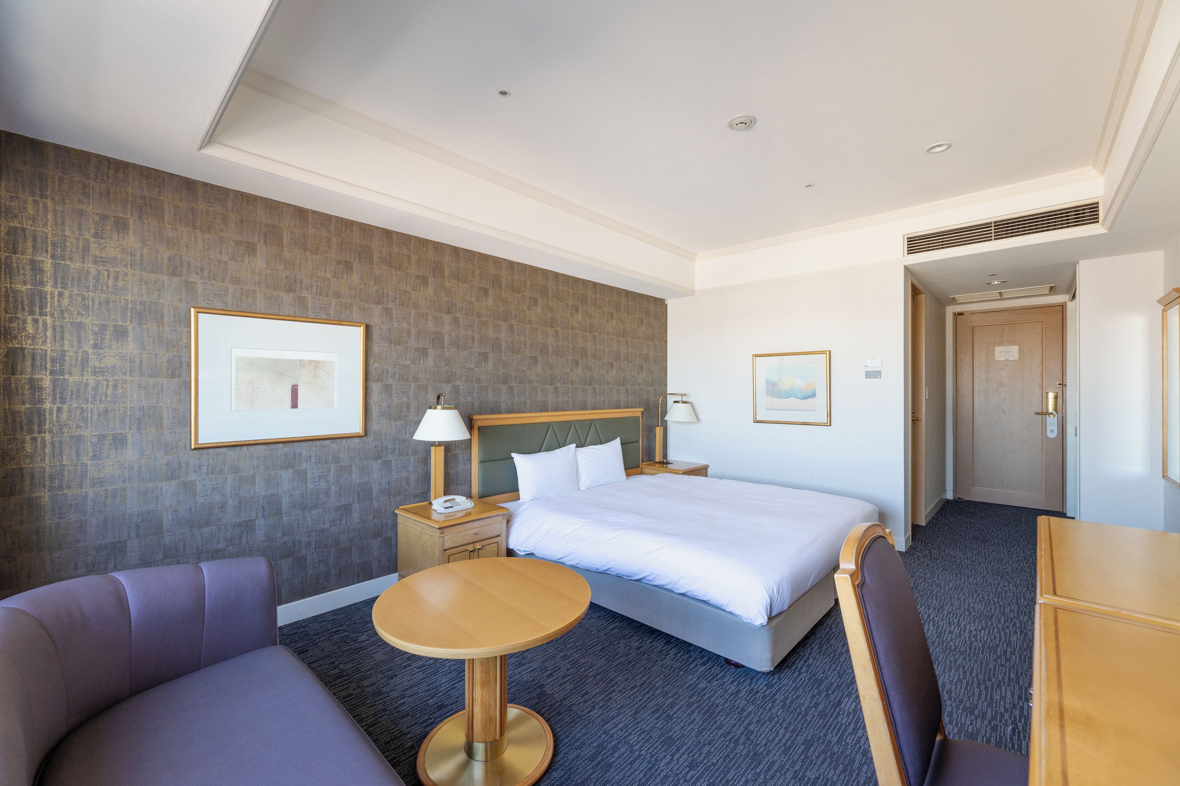 Une chambre d’hôtel avec un lit, une table ronde, un canapé et une table de chevet avec une lampe.