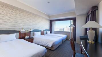 A hotel room with three beds, a desk, a chair, a lamp, and a view of the city.