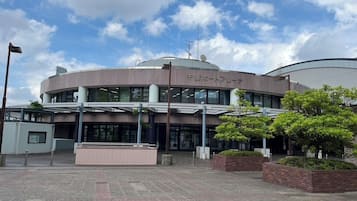 Een modern gebouw met een rond centraal deel en een plat dak, omgeven door een verhard gebied met plantenbakken en een vlaggenmast.