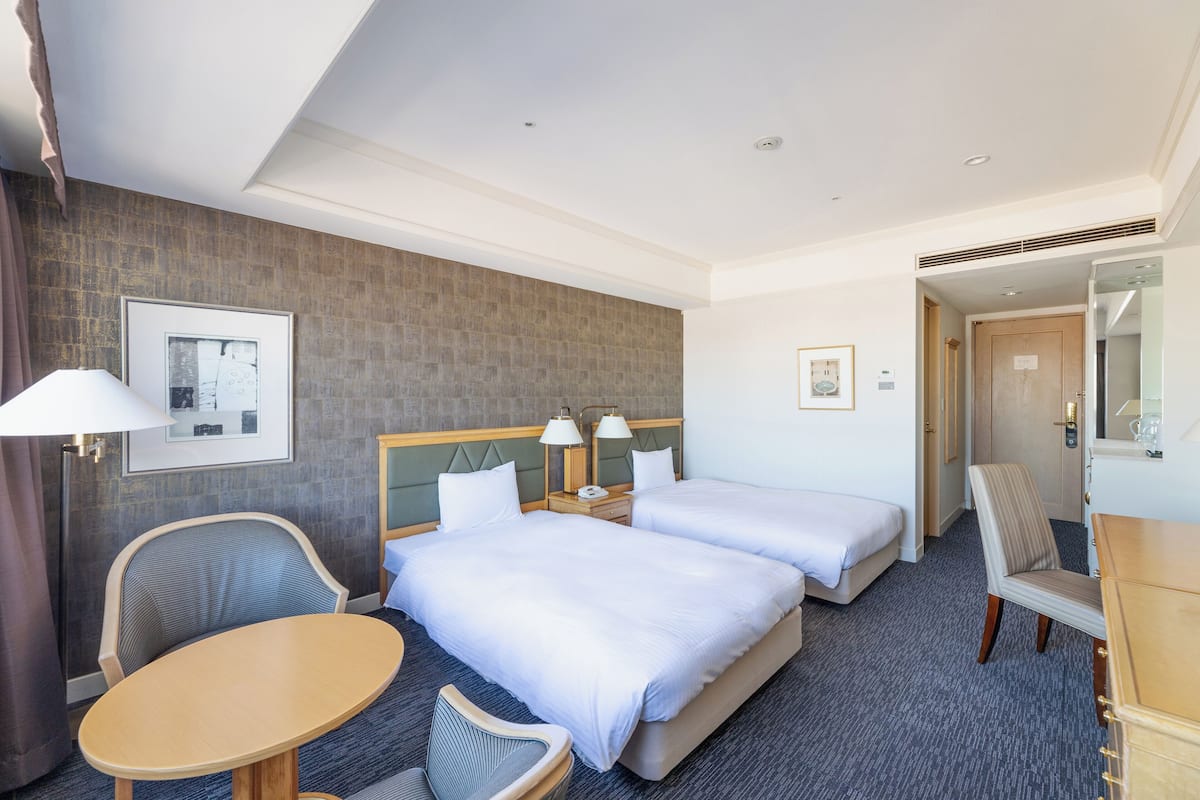 Une chambre d’hôtel avec deux lits, un bureau, une chaise, une table et un miroir.