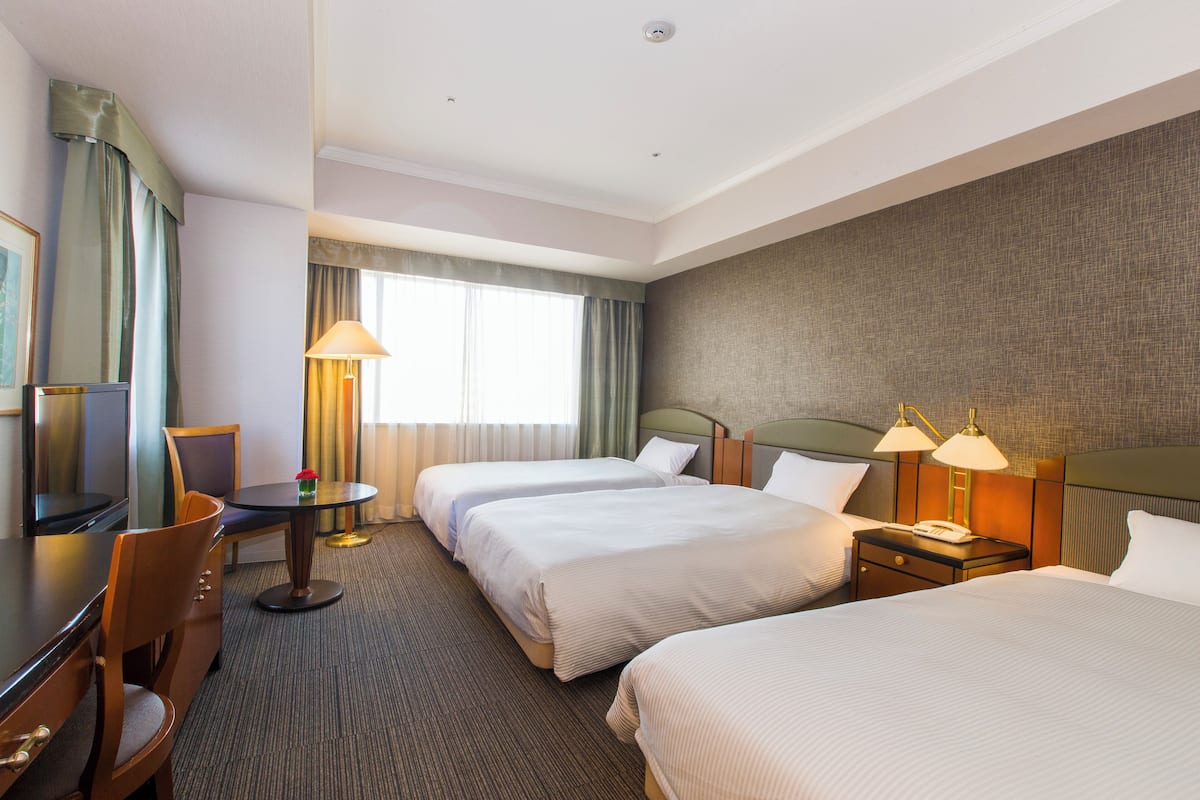 Une chambre d’hôtel avec deux lits, un bureau, une chaise, une lampe et un téléviseur.