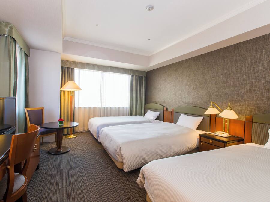 Quarto de hotel com duas camas, uma escrivaninha, uma cadeira, um abajur e uma televisão.