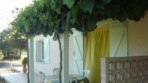 Un’area salotto esterna coperta con tavolo e sedie, una pianta in vaso e una tenda gialla.