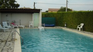 Una piscina con bordo in pietra, qualche sedia a sdraio e un piccolo edificio sullo sfondo.