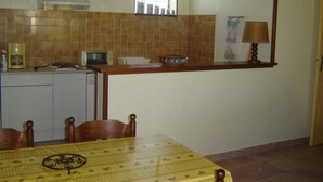 Una cucina compatta con forno a microonde, tostapane e macchina del caffè sul piano di lavoro. C'è un tavolo da pranzo con sedie e una lampada sul bancone.