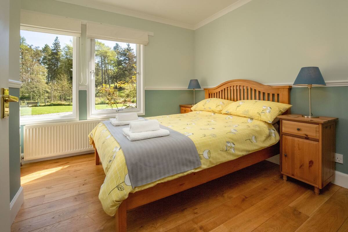 Une chambre à coucher avec un lit, deux tables de chevet, une fenêtre et une vue sur un parc.