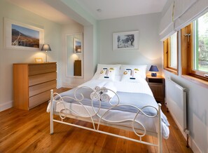 A neatly arranged bedroom with a bed, wooden dresser, and framed pictures on the walls.