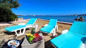Eine Strandlounge mit weißen Liegestühlen und einem Korbstuhl-Tisch mit Obst und Brot.