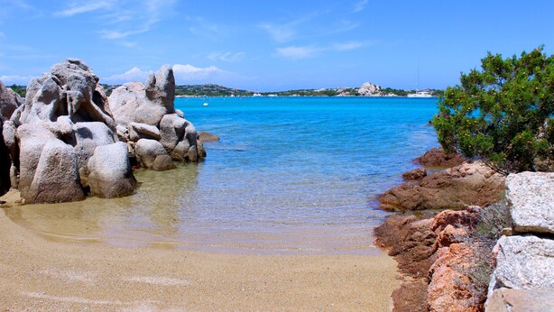 Ein Strand mit klarem, blauem Wasser, Felsformationen und grüner Vegetation.