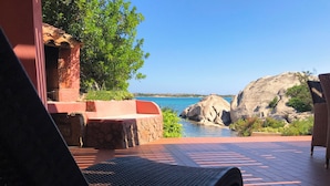 En terrasse med en fletstol, en stenvæg og havudsigt over klipper.