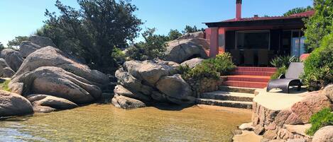 A house with a red roof, large rocks, and a clear water feature.