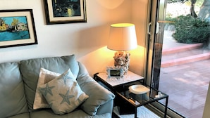 En stue med en grå sofa, søstjerne-puder, en lampe og et lille bord med en fjernbetjening.