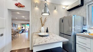 A modern kitchen with a marble countertop, stainless steel appliances, and a view into the dining area.