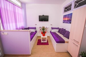 Un espacio habitable compacto con kitchenette, televisor de pantalla plana y cama con ropa de cama morada.