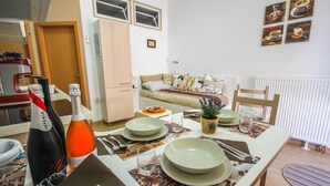 Ein Essbereich mit Tisch für vier Personen, eine Couch im Hintergrund und eine Küche zur Linke.