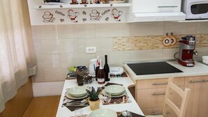 Eine kompakte Küche mit Esstisch für zwei Personen, einer Mikrowelle, einer Kaffeemaschine und einem Fernseher, der über der Arbeitsfläche angebracht ist.